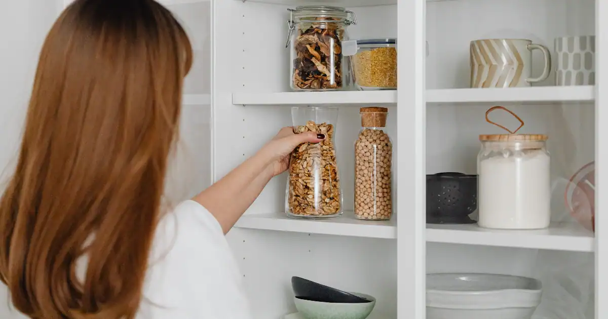 Woman organizing pantry jars and kitchen essentials on white closet shelving for a clean functional space